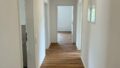 Heller, moderner Flur mit Holzfußboden und weißen Wänden in einer Erdgeschosswohnung.