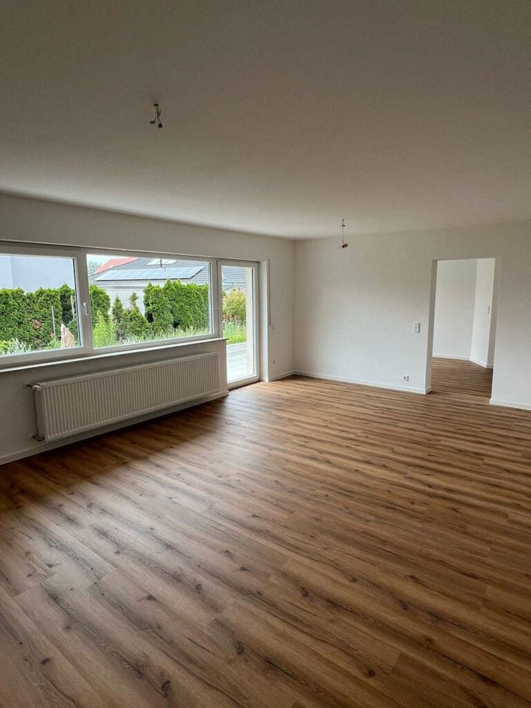 Helles, leerstehendes Wohnzimmer mit großen Fenstern, Parkettboden und Zugang zum Garten.